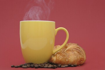 Steaming coffee cup with coffee beans and a croissant
