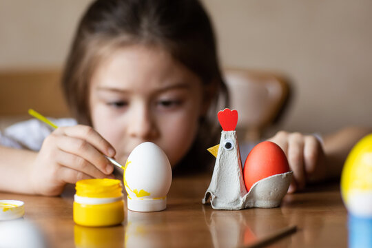 child paints eggs for Easter at home at table. kids craft - egg stand made from packaging carton