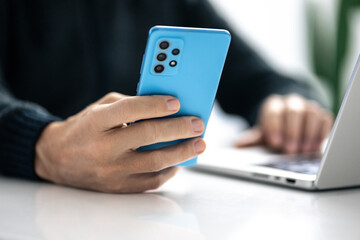 Closeup image of a male hands using smartphone and laptop. Boy working online, internet applications