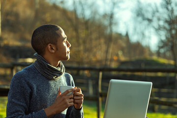 Young freelancer enjoying a coffee break in nature with laptop