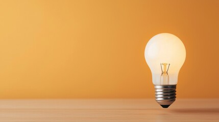 Glowing light bulb on a wooden surface with a warm orange background, representing innovation and bright ideas.