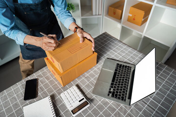 Elderly man labeling packages while working at a desk with a laptop