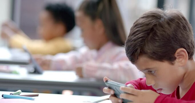 In school, children using tablets and smartphones in classroom, focusing on screens