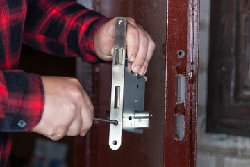 A male locksmith installs a new door lock on a metal door.