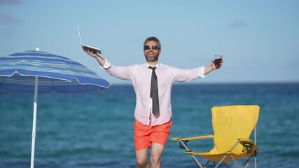 Excited businessman working on a laptop by the sea. A man enjoying a tropical beach while working online. A freelancer typing on a laptop under the sun beach. A businessman on vacation.