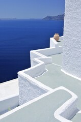 Fototapeta premium Angled terrace with a gray floor and white walls, yellow clay vase, in front of the blue sea, Oia, Ia, Santorini, Cyclades, Greece, Europe