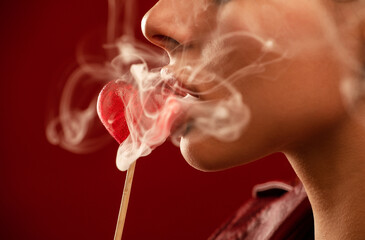 A sexy girl with beautiful makeup in a red leather jacket holds a candy in the shape of a heart on...