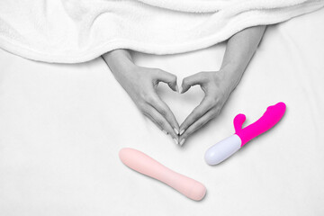 The girl is lying in a white bed. A woman holds a pink dildo in her hand. Toys for adults.
