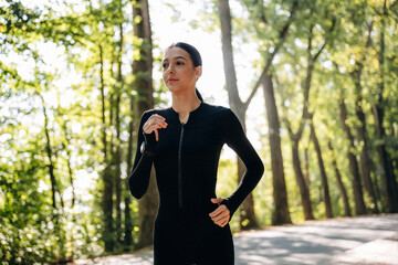 Running, jogging in the forest. Young sportive skinny woman is in black fitness clothes outdoors