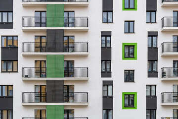 Modern apartment buildings with white facades and green accents, windows and balconies with metal railings against cloudy sky, front view