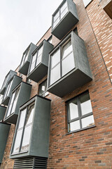 Contemporary apartment facade with multicolored brick walls, windows, and protruding gray balconies. Urban housing concept, low angle view
