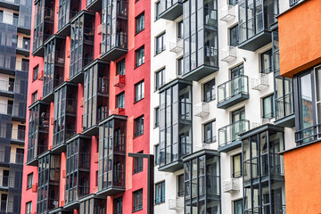Contemporary apartment buildings with orange, white, and red facades, featuring numerous balconies with dark-framed windows. Urban housing concept