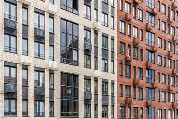 Fototapeta premium Contemporary multi-story buildings with beige, red brick and glass facades, showcasing balconies and windows. Urban architecture concept