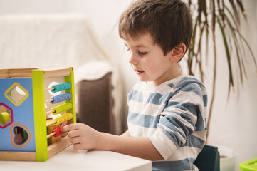 5 year old boy learning to count on colored wooden abacus. Child development and preschool...
