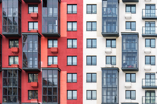 Contemporary apartment buildings with beige and red facades, featuring numerous balconies with dark-framed windows. Urban housing concept, front view