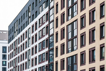 Modern multi-story apartment building with contrasting colors and large dark-framed windows. Urban residential concept