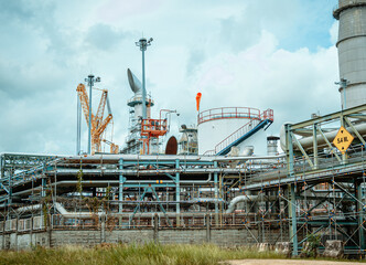 Naklejka premium Industrial facility with smokestacks and flaring gases under a cloudy sky in a coastal area