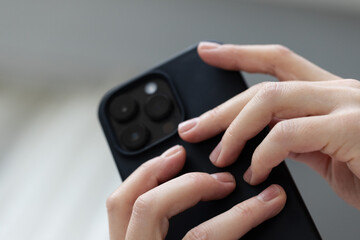 Fototapeta premium Black smartphone in the female hands. Low angle, closeup.