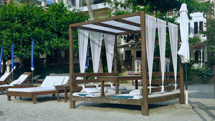 Beach resort bed shelter on a tropical island. One open gazebo with curtains pillow and bedding on the sand on the beach. Luxury lounge with sun chair and white curtains 