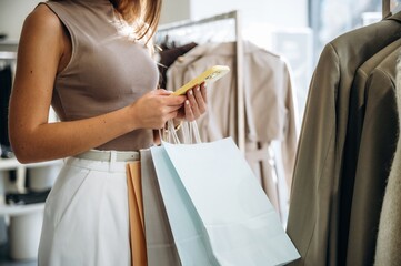 Smartphone in hands. Close up view of woman that is chooses clothes in the retail shop