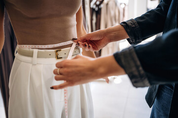 Fototapeta premium Measuring the waist. Two female friends are in the retail store, choosing clothes, shopping