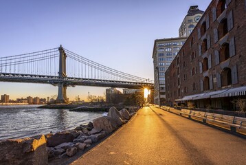 Fototapeta premium Manhattan Bridge in Backlight, Morning Sun, Sun Star, Sunrise, Empire Fulton Ferry Park, Dumbo, Brooklyn, New York, USA, North America