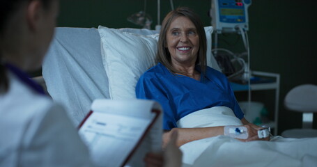 Young doctor, seated beside the elderly patient, extends a document for her signature.