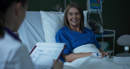 Obraz premium Young doctor, seated beside the elderly patient, extends a document for her signature.