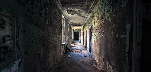 Obraz premium Long derelict corridor with crumbling walls and light flooding from broken windows. Symbolic of forgotten paths, isolation, and complexity of life journey through time.