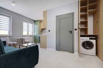 Salon w nowoczesnym apartamencie z seledynowym aneksem kuchennym z ciemnozieloną sofą © arteffect.pl