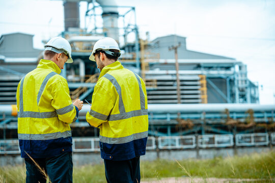 Engineers discuss details while inspecting machinery at an industrial facility during the day