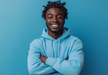 Obraz premium A portrait of an African American man in a blue sweatshirt, smiling with his arms crossed against a vibrant blue background.
