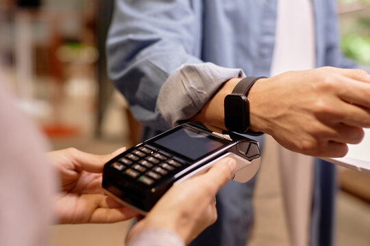 Close-up image of man's hand using smartwatch for contactless payment at a store checkout counter, demonstrating convenience and modern technology in everyday transactions