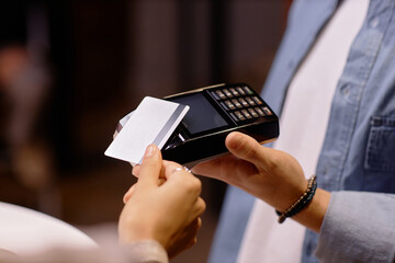 Person holding card while conducting transaction with a card scanner device in a retail environment. Close-up capture showing detalles of hands, card, and payment device