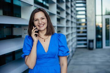 Fototapeta premium A young businesswoman is talking on the phone against the background of an industrial city building. Close up, copy space