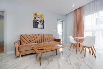 Salon w nowoczesnym apartamencie z beżowym  aneksem kuchennym z rudą jasno brązową pluszową sofą