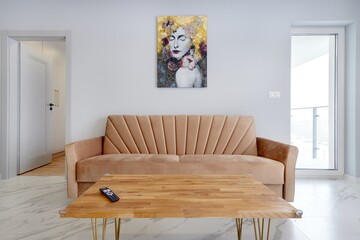 Salon w nowoczesnym apartamencie z beżowym  aneksem kuchennym z rudą jasno brązową pluszową sofą © arteffect.pl