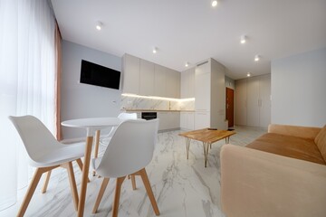 Salon w nowoczesnym apartamencie z beżowym  aneksem kuchennym z rudą jasno brązową pluszową sofą