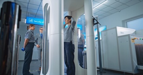Diverse People Passing Through Metal Detector Gates in Airport Terminal. Security Officer Controls Inspection of Passengers for Plane Flight. Group of Travelers Going on Vacation Trips. Handheld. © Framestock