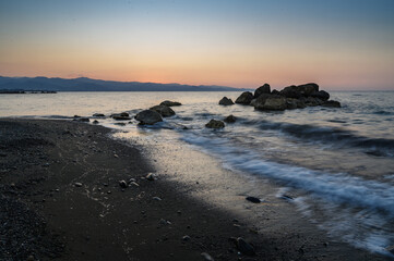 Calm waves lap against rocky shore at dusk near tranquil coastline