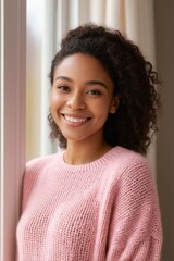 smiling woman in pink sweater standing by window with white curtains
