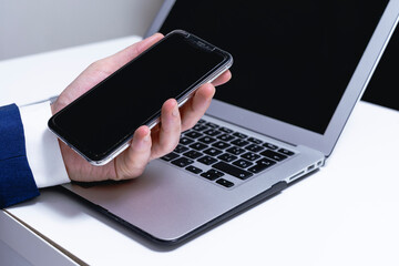 businessman hand holding smart phone with blank screen on laptop computer background