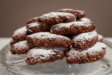Traditional Italian Pan dei Morti cookies made with dried fruits, nuts, cocoa, and spices, dusted with powdered sugar, displayed on a glass platter, associated with All Souls Day