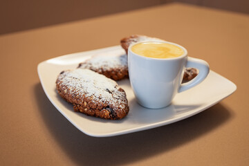 Pan dei Morti cookies dusted with powdered sugar served alongside a cup of creamy caffe macchiato, a classic Italian pairing for an indulgent snack