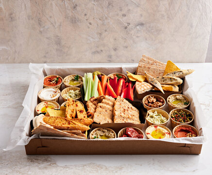 A lavish spread of savory dips, fresh vegetables, and various breads is artistically arranged on a wooden table, creating an inviting and colorful appetizer display for gatherings
