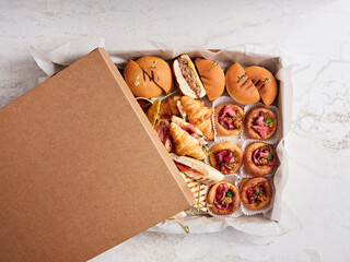 A takeout box filled with a variety of gourmet sliders and pastries, showcasing rich flavors and careful presentation, ideal for an event or gathering with friends and family