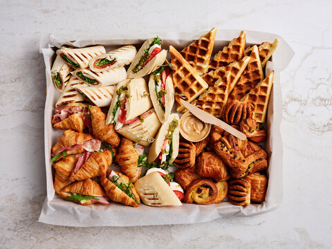 An assortment of delicious food items is arranged on a tray, featuring sandwiches, waffles, and pastries, perfect for a brunch gathering or celebration. Guests can enjoy a flavorful selection