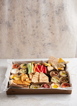 A colorful platter is filled with an assortment of dips, crunchy chips, and fresh vegetable sticks arranged neatly on a wooden tray. Perfect for sharing at parties or gatherings