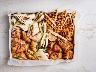 A vibrant brunch display showcases a variety of delicious food items including croissants, wraps filled with fresh ingredients, and crispy waffles arranged on parchment