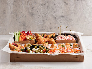 A tray filled with a variety of appetizers including shrimp, croissants, vegetables, and olives, set against a neutral background, ideal for parties or celebrations